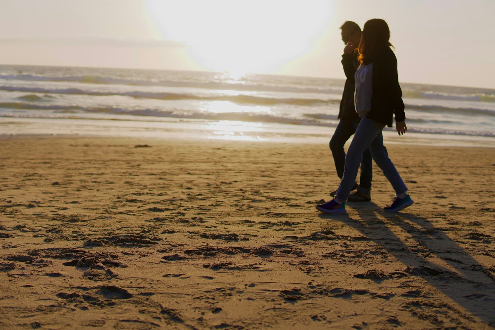 A couple in casual clothes walking along a beach at sunset, seen from behind